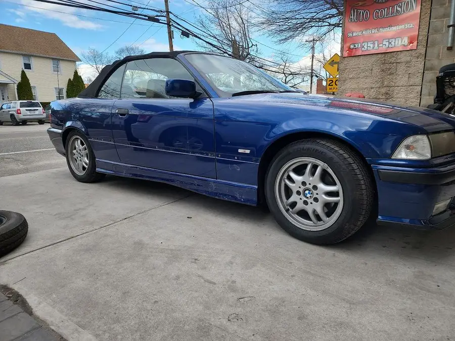 Blue BMW convertible parked on the concrete lot beside a red auto collision sign
